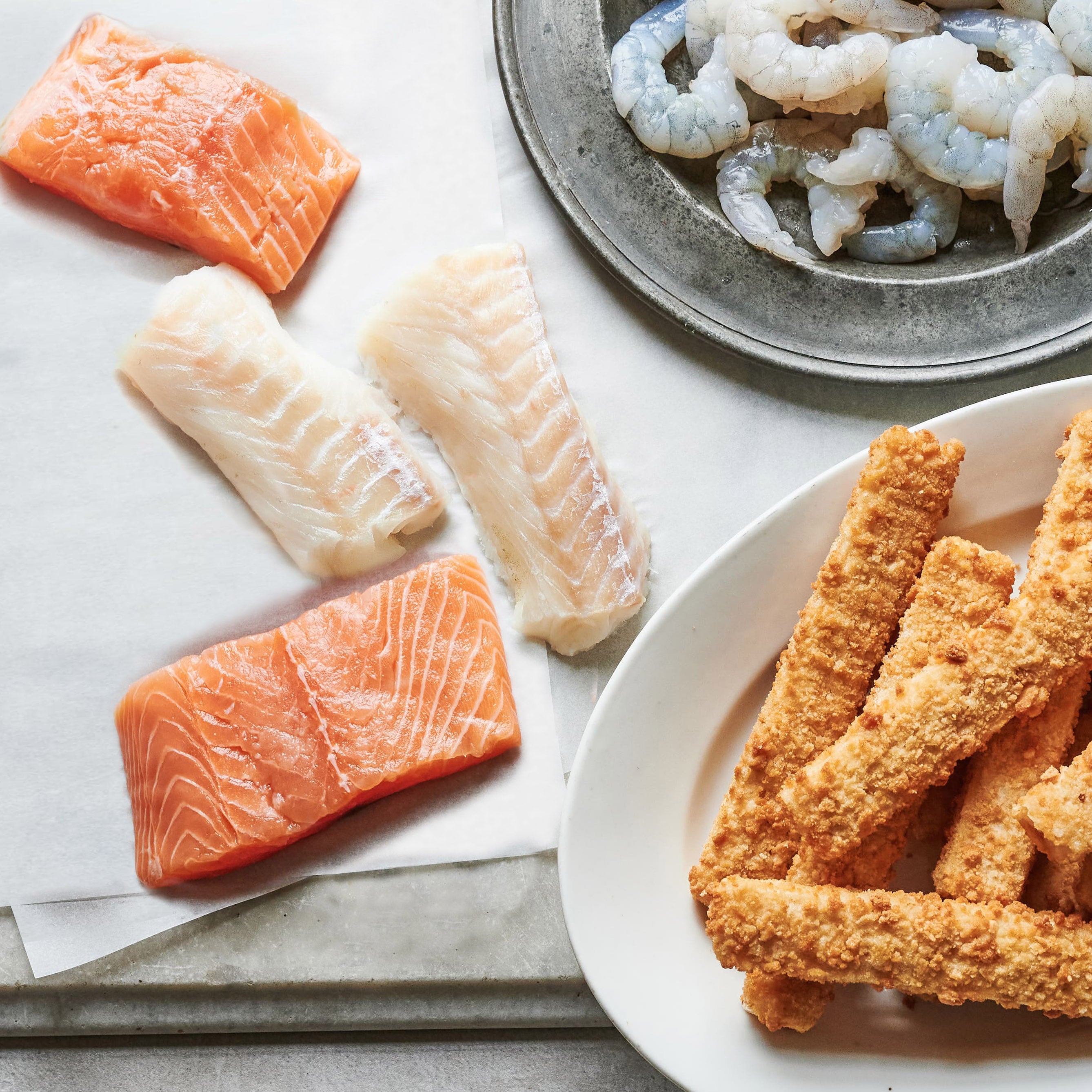 Tom the Fish - Assorted seafood including salmon fillets, cod loins, king prawns, and breaded fish fingers arranged on a table.