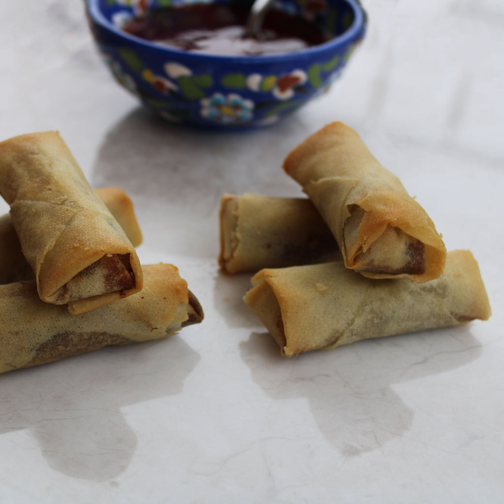 Crispy Duck Spring Rolls on a plate with sweet and sour sauce in a small bowl on the side.